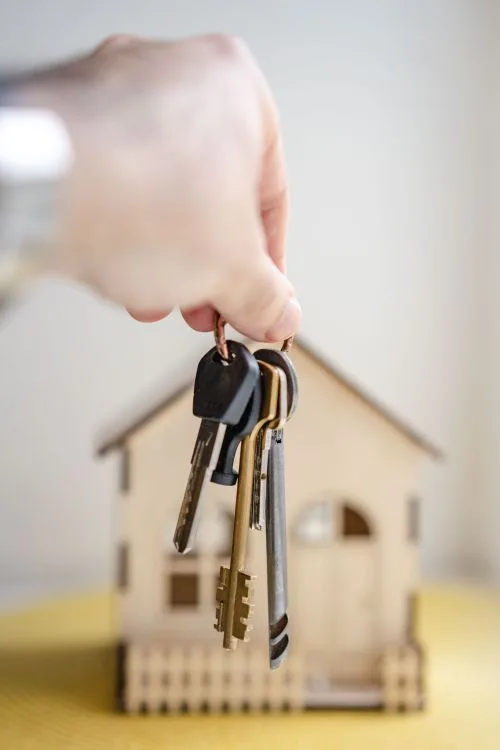Persona sosteniendo llaves de casa frente a una vivienda en miniatura, simbolizando la compra de un hogar