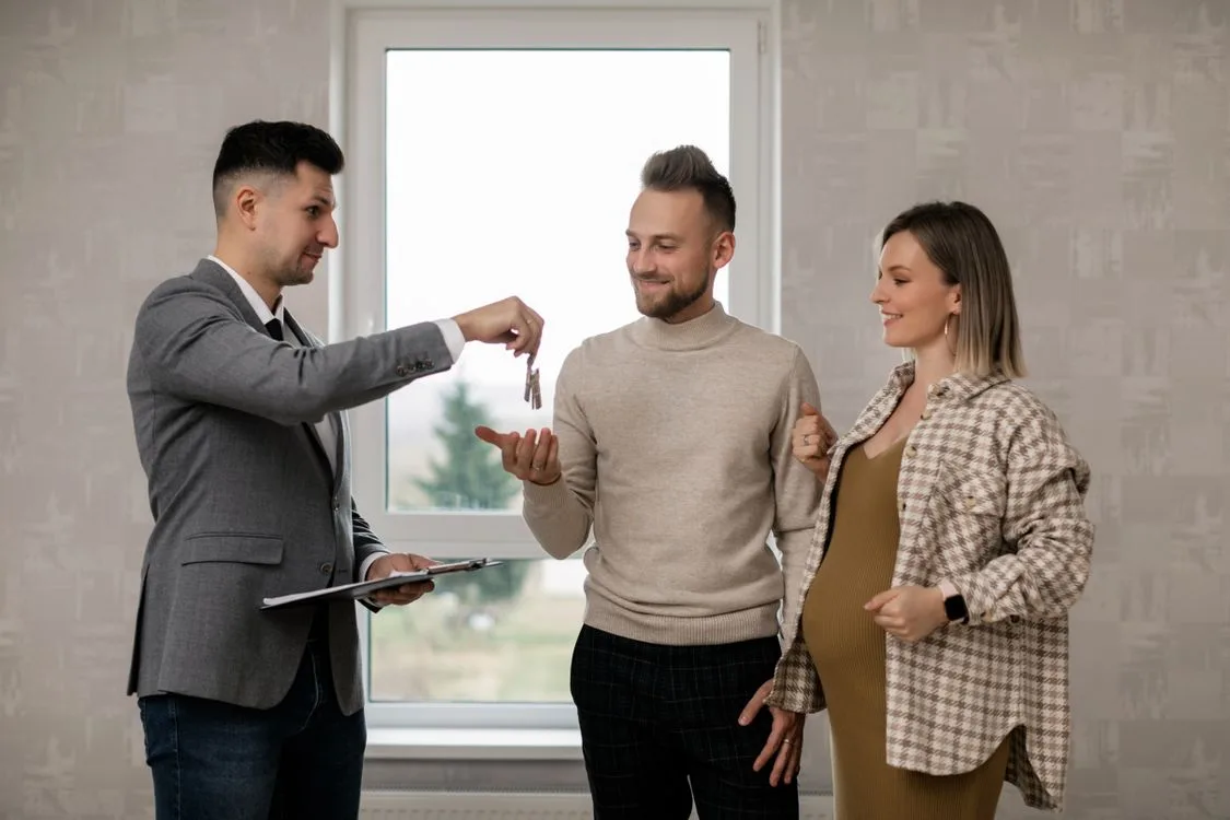 Agente inmobiliario entregando las llaves de una casa nueva a una pareja de compradores